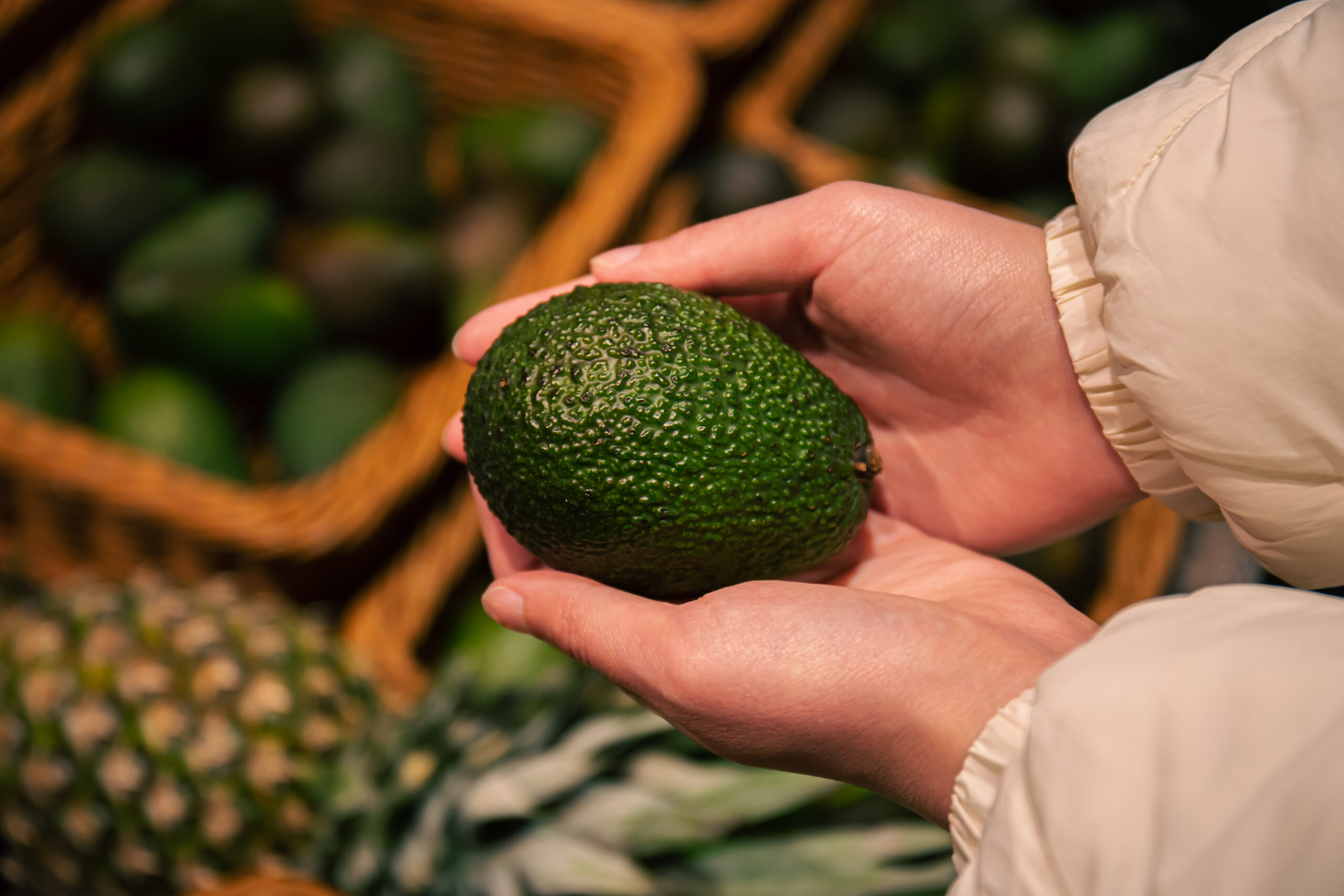 A woman chooses an avocado in a grocery store, close-up, buying organic food for cooking.