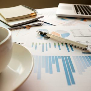 Business concept with copy space. Office desk table with pen focus and analysis chart, computer, notebook, cup of coffee on desk.Vintage tone Retro filter, selective focus.