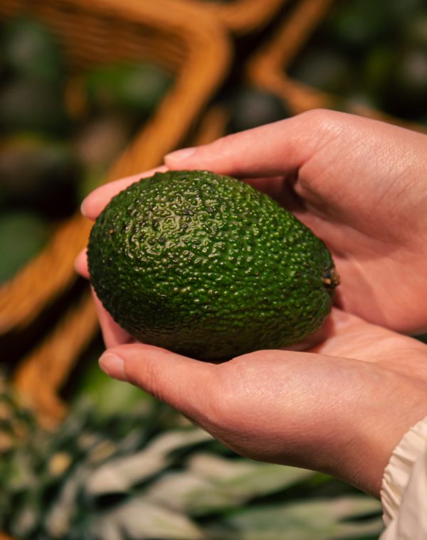 A woman chooses an avocado in a grocery store, close-up, buying organic food for cooking.